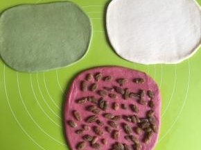 取出面团每一份都擀扁仔细排出气体，葡萄干提前用清水泡一下，沥干水，把葡萄干铺匀在红色面团上