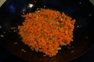 炒锅中倒少许油，葱花煸炒出香味后 ，将胡萝卜丁入锅中煸炒变色