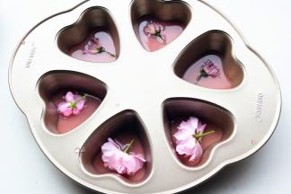 把用来做镜面的那部分草莓吉利丁溶液，倒一半到学厨六连心形模内，再放上一朵樱花，然后放入冰箱冷藏40分钟，等凝固。我还用了三朵盐渍樱花，盐渍樱花比较咸，一定要多浸泡清洗几次去除盐分。