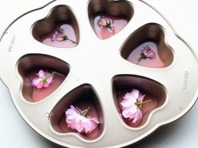 把用来做镜面的那部分草莓吉利丁溶液，倒一半到学厨六连心形模内，再放上一朵樱花，然后放入冰箱冷藏40分钟，等凝固。我还用了三朵盐渍樱花，盐渍樱花比较咸，一定要多浸泡清洗几次去除盐分。