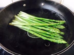 锅里放水，水开了后，放入1小勺盐、2滴炒菜油，放入芦笋，大火煮开，煮约2分钟左右，捞出来过凉水，沥干水分备用。