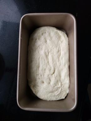 用刮刀反复折叠面团，帮助面团排气。再将面团移入抹油的模具中，并拉伸至模具大小。