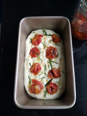 用手指在面团上轻轻地戳一个个小凹陷，淋上橄榄油，放上油浸小番茄，撒上迷迭香。