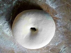 面板上撒上适量干粉，把面团揉圆，中间掏洞，双手绕着洞把面团拉细