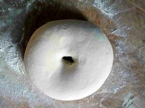 面板上撒上适量干粉，把面团揉圆，中间掏洞，双手绕着洞把面团拉细