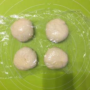 第一次发酵好的面团放在揉面垫上先揉压排出气体，分成大小相等的四份小面团，揉圆，盖上保鲜膜醒发15分钟