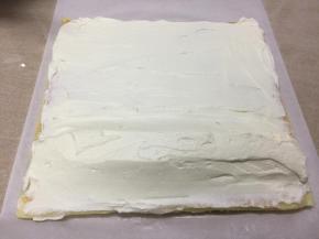 将奶油抹在蛋糕片上，起始端要多留一些，堆成小山状