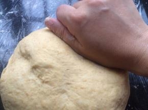 把面团拿出操作台上用手轻轻按压排气。