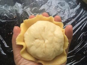 把压成薄饼状的菠萝皮轻轻移到手掌心，放入包了菠萝馅的面团、把边边的菠萝皮往面团里收一收即可。