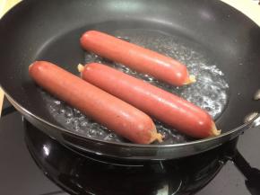 4. 在平底锅中放入热狗肠，倒入50毫升水
盖上盖子调至中火，待水蒸发完，热狗肠表皮焦黄时关火