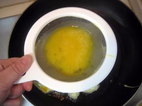 烧至八成热时，将蛋液由漏勺淋到油中； 快速用筷子在将蛋液划散，不要让蛋液结块；