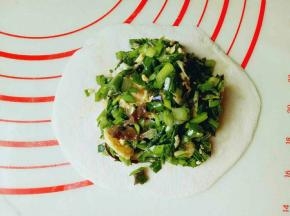 取一块面团，用擀面杖擀圆饼，包上韭菜鸡蛋馅。