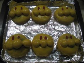 将面包生胚放温暖处发酵，发酵结束后表面刷全蛋液，每个面团上放两粒枸杞子（或葡萄干）做眼睛。烤箱预热180度，中层，烤20分钟。