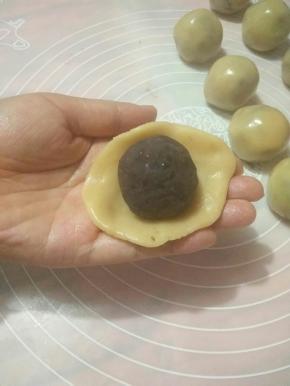 取一面团压扁成圆形放置掌心，放入豆沙馅，利用虎口往上推，捏紧收口。