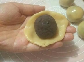 取一面团压扁成圆形放置掌心，放入豆沙馅，利用虎口往上推，捏紧收口。