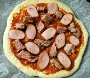 烤好的饼底先抹上番茄牛肉酱，再放上煎好切块的牛排和脆皮肠