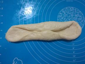 7、	取出其中一个面团，擀成长舌状。两边往中间对折，稍微压扁。