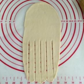 取一个松弛好的面团，擀成长型，下端擀的薄些，然后用刮板在下端切5刀。