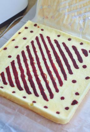 蛋糕表面铺一张油纸，将蛋糕放在案板上反转过来，小心撕扯有条纹一面的油纸。上面虚盖一张油纸，将蛋糕放凉。