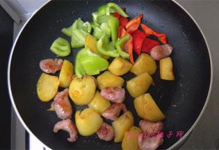 待香肠块和土豆块煎至上色后，倒入青椒和彩椒块；