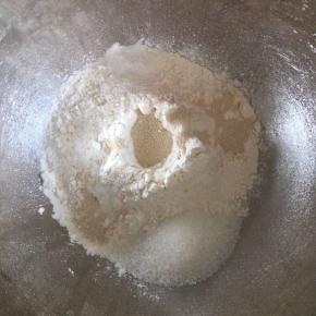 先来做汉堡包，高筋面粉倒入碗内，面粉中间挖一个坑，倒入活性干酵母，细砂糖和盐对角线放，蛋液倒入