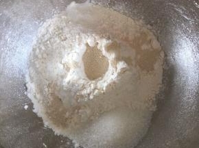 先来做汉堡包，高筋面粉倒入碗内，面粉中间挖一个坑，倒入活性干酵母，细砂糖和盐对角线放，蛋液倒入