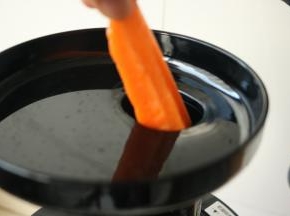 启动原汁机，把胡萝卜条从投料口投入机器。