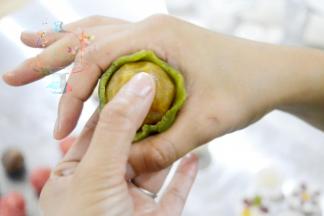 取一个桃山皮，在手掌上按压扁之后，图示这样的手法。一只手的拇指和其余四指托住皮和馅儿，另外一只手用虎口位置向上收紧包圆