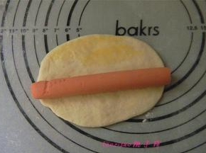 擀好的牛舌状的面片上放上一根火腿肠，在面片的长边刷少许蛋液（刷蛋液的目的是为了在封口时起到粘合的作用）；