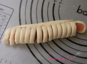 将面片的长边卷起将火腿肠包在里面，用刀切出均等的小段（注意：另一端面片不要切断）；