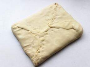 冻好的面团拿出来，擀成黄油块大小的两倍大，把黄油片包在里面。四周捏紧，紧紧包住黄油。