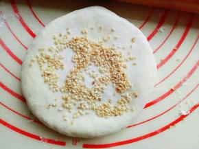 放一些芝麻在饼上面，用擀面杖来回擀，擀薄。