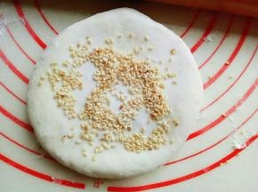 放一些芝麻在饼上面，用擀面杖来回擀，擀薄。