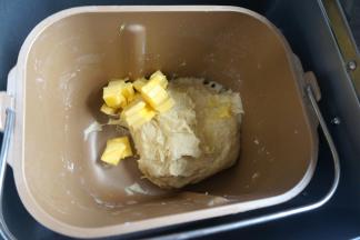 待面团揉得能扯出较厚的膜时，加入软化的黄油，继续揉面；夏天温度高，建议开着面包机的盖子来揉面，这样也能将一部分热量释放出去，在面团还没形成筋度前不会让面团快速发酵