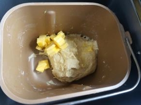 待面团揉得能扯出较厚的膜时，加入软化的黄油，继续揉面；夏天温度高，建议开着面包机的盖子来揉面，这样也能将一部分热量释放出去，在面团还没形成筋度前不会让面团快速发酵