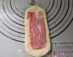 取一面团，擀成牛舌状，铺上培根片，从一端卷起封口朝下；