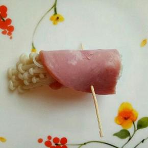 取一片火腿，放入金针菇卷起来，用牙签扎透即可，如图，依次做完。