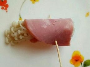 取一片火腿，放入金针菇卷起来，用牙签扎透即可，如图，依次做完。