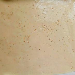 把打面糊倒入铺有油纸的烤盘中，用刮板刮平整，撒上白芝麻，会很香哦。