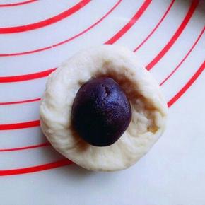 发酵好的面团从面包机取出，盖上保鲜膜排气10分钟，再分割成小面团，每个约50g，面团压扁包上豆沙馅，收口朝下。