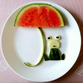 切一片西瓜放在陶玻网的大白盘子里，（这款盘子绝对是做拼盘的最佳选择），然后把青蛙的各部分组合到一起，可以把青蛙的脸部下方切去一部分，这样可以和身体的部分贴合的更好。用西瓜籽做青蛙的眼睛和嘴，嘴巴的部分是半个西瓜籽。