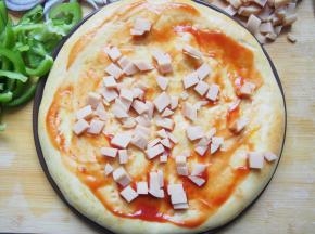 烤好的饼胚上刷一层番茄酱，洒上切碎的鸡肉肠