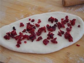 取其中的一块擀成椭圆形，放入切碎的蔓越莓，从一端卷起，收口朝下放入吐司模。