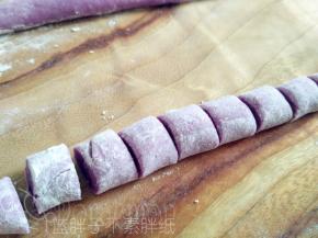 案板上撒上玉米淀粉，取出一小团紫薯味面团，将它搓成长条，然后用刀切成小块。