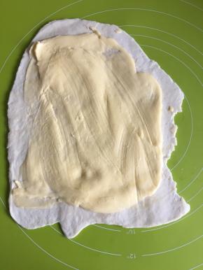 取出面团，擀面杖擀成长方形状，把裹入用的70g黄油稍微软化后压扁放在面皮上