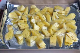 在烤盘中垫一张锡纸，方便后期清洁，将土豆块均匀的放置烤盘中，放入蒜片。