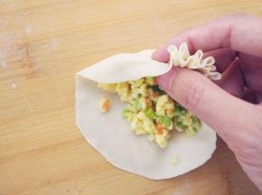 左手托底，在右手捏褶的同时，慢慢转动，且用左手拇指将馅料不断向内压，这样可以包入更多馅料。右手用拇指食指不断将面片边缘均匀折叠，用剩余几指在边缘下方压实。距离边缘越远，花瓣越大，反之则越小