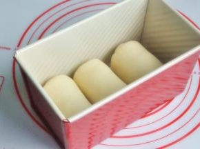 再次擀开成长条状，面团卷起，收口朝下放置，将面团放入吐司模。