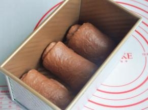 将面团擀开卷成圆筒状，3个都做同样处理，盖上保鲜膜静置15分钟左右，再次擀开成长条状，面团卷起，收口朝下放置，将面团放入吐司模。