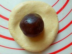 取一块面团，用手掌心按扁，放上豆沙馅。(每个面团约50g，豆沙馅每个约20g)